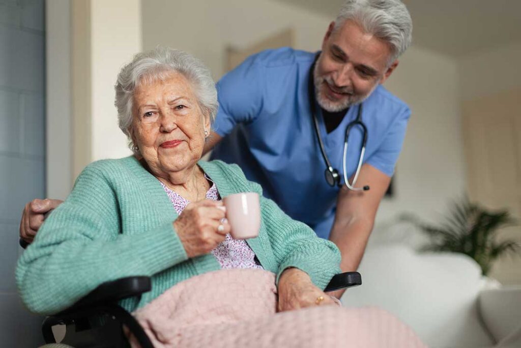A caregiver and an older adult reviewing a pill organizer together at a kitchen table.